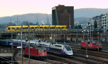 Tango tram crosses the tracks of Basel SBB station, when a TGV 2N2 (Euroduplex) arrives from Zurich.